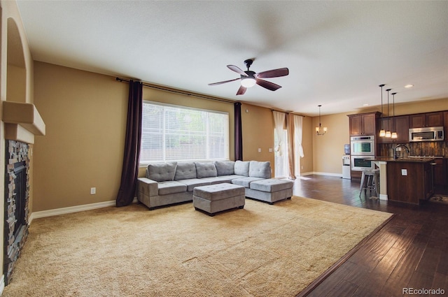 living area featuring baseboards, ceiling fan with notable chandelier, recessed lighting, and a stone fireplace