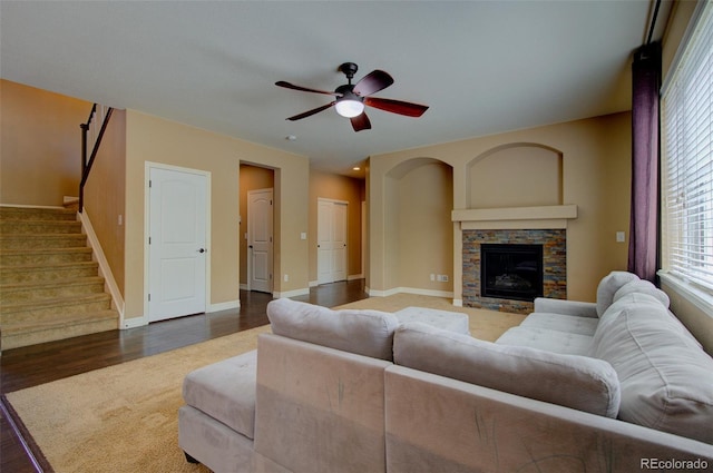 living area with ceiling fan, a stone fireplace, wood finished floors, stairway, and baseboards