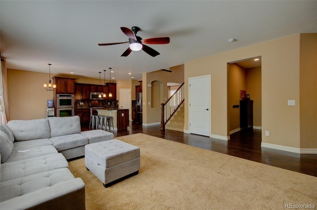 living area featuring arched walkways, baseboards, ceiling fan with notable chandelier, dark wood-style floors, and dark carpet