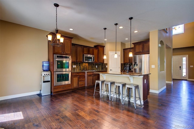 kitchen featuring baseboards, dark wood finished floors, appliances with stainless steel finishes, and a kitchen bar