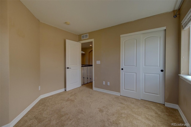 unfurnished bedroom with baseboards, visible vents, light carpet, and a closet