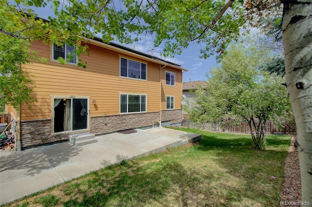 back of house with a patio area, fence, a yard, and stone siding