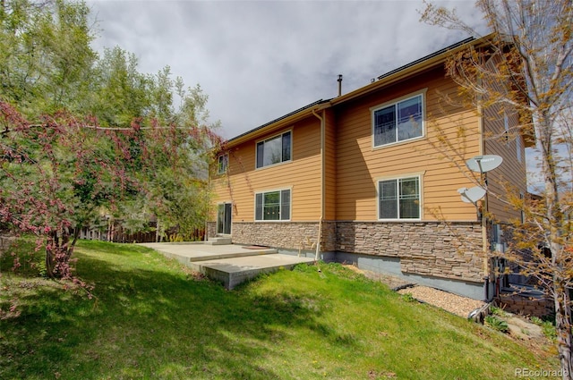 rear view of house with a lawn, stone siding, and a patio area