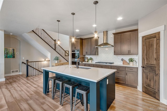 6093 Carmon Dr, Windsor, CO 80550 - kitchen with visible vents, wall chimney range hood, a sink, light wood finished floors, and stainless steel appliances