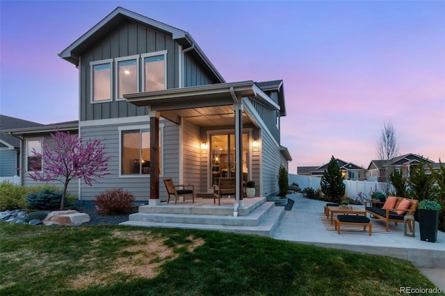 6093 Carmon Dr, Windsor, CO 80550 - back of property at dusk featuring board and batten siding, a lawn, a patio area, fence, and an outdoor hangout area