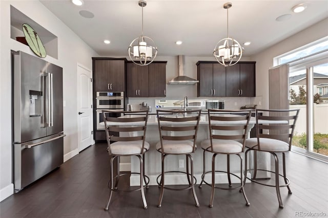 4504 N Picadilly Ct, Aurora, CO 80019 - kitchen with stainless steel appliances, wall chimney range hood, a chandelier, dark brown cabinetry, and recessed lighting