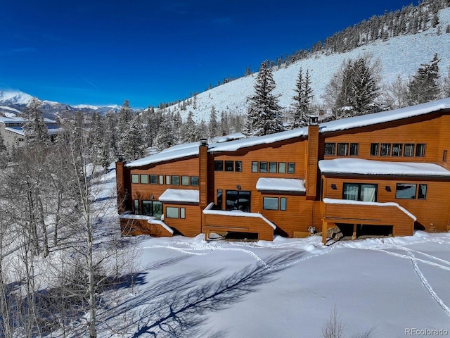 snow covered house with a mountain view and a chimney