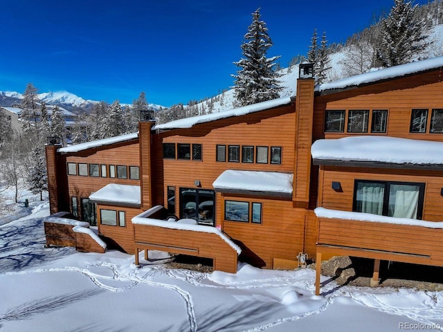 snow covered rear of property featuring a chimney and a mountain view