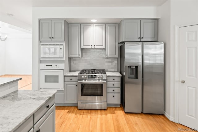 kitchen featuring appliances with stainless steel finishes, gray cabinetry, backsplash, light wood-style flooring, and light stone counters