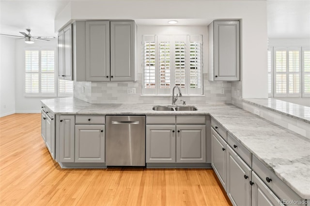 kitchen featuring gray cabinets, stainless steel dishwasher, a sink, ceiling fan, and light wood-style floors