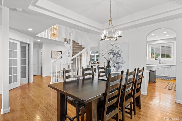 16862 W 65th Cir, Arvada, CO 80007 - dining space with a chandelier, stairway, light wood-style flooring, a raised ceiling, and arched walkways