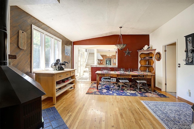 dining room featuring lofted ceiling, wood walls, light wood-type flooring, and a textured ceiling