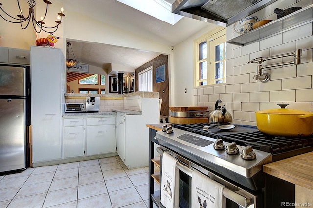 kitchen with light tile patterned floors, stainless steel appliances, decorative backsplash, lofted ceiling, and white cabinets