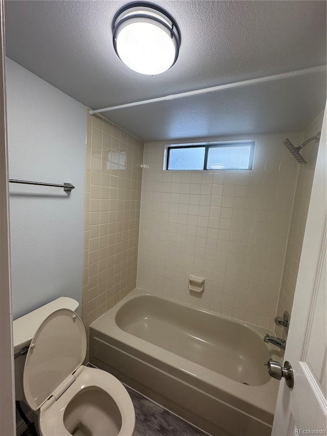 bathroom with a textured ceiling, shower / bathtub combination, and toilet