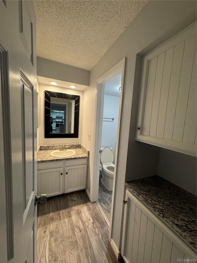 bathroom featuring toilet, a textured ceiling, wood-type flooring, and vanity