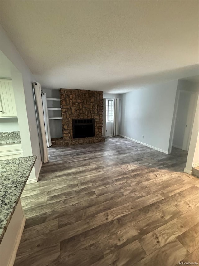 unfurnished living room with dark wood-type flooring, a textured ceiling, and a stone fireplace