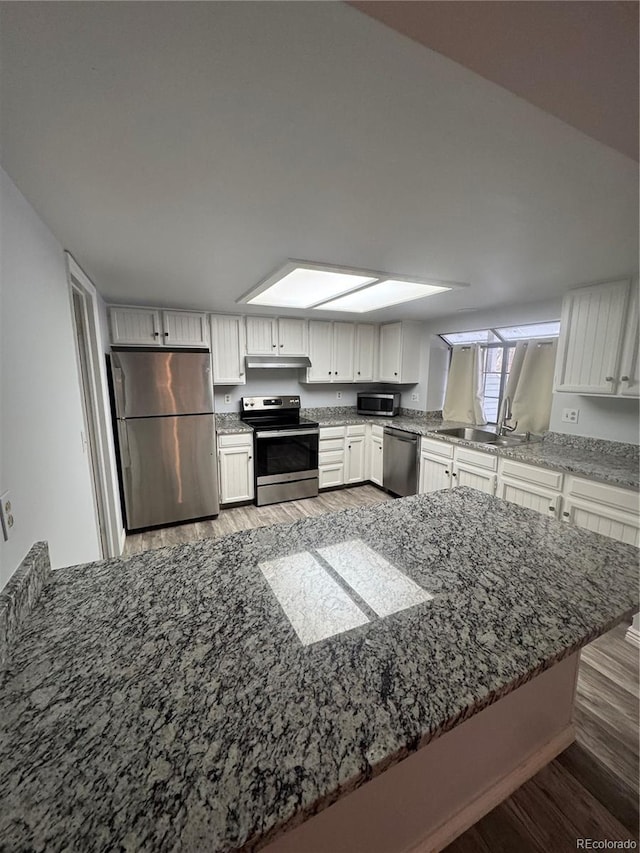 kitchen with stainless steel appliances, kitchen peninsula, dark hardwood / wood-style floors, white cabinets, and sink