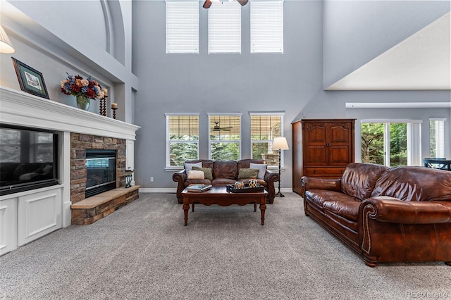 carpeted living room featuring ceiling fan, a towering ceiling, a fireplace, and a healthy amount of sunlight