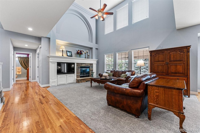 living room with ceiling fan, a stone fireplace, and light hardwood / wood-style flooring