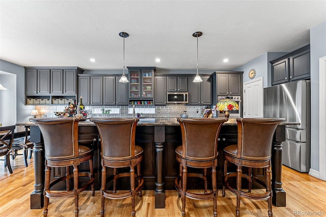 kitchen with hanging light fixtures, an island with sink, appliances with stainless steel finishes, and gray cabinetry