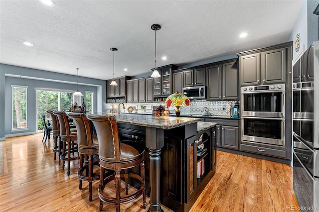 kitchen with appliances with stainless steel finishes, a breakfast bar, an island with sink, dark stone counters, and hanging light fixtures