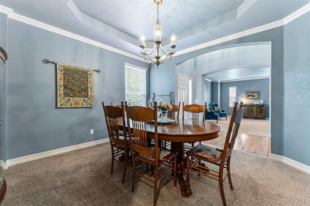 carpeted dining space featuring crown molding, an inviting chandelier, and a tray ceiling