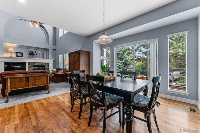 dining room with ceiling fan, a stone fireplace, and light wood-type flooring