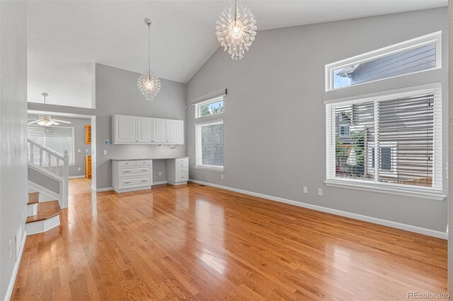 unfurnished living room featuring high vaulted ceiling, light hardwood / wood-style floors, and ceiling fan with notable chandelier