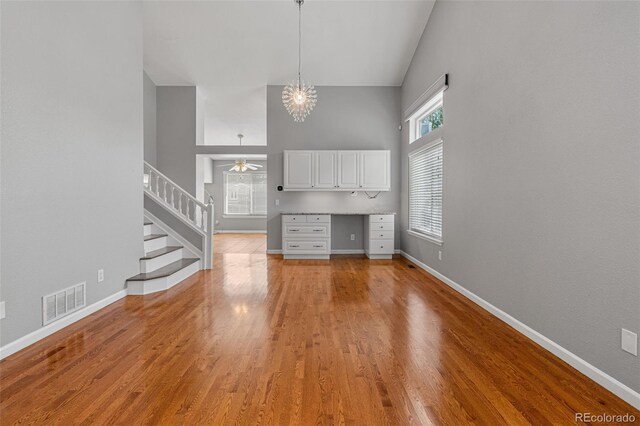 unfurnished living room with ceiling fan with notable chandelier, a high ceiling, and light hardwood / wood-style flooring