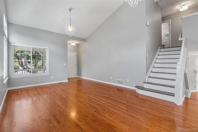 unfurnished living room with lofted ceiling, an inviting chandelier, and light wood-type flooring