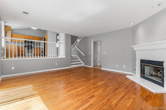 unfurnished living room with light wood-type flooring, lofted ceiling, and a stone fireplace