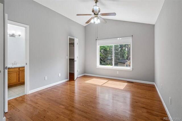 unfurnished bedroom featuring ceiling fan, light wood-type flooring, a walk in closet, vaulted ceiling, and connected bathroom