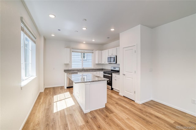 kitchen with a center island, light stone countertops, light hardwood / wood-style floors, white cabinetry, and stainless steel appliances