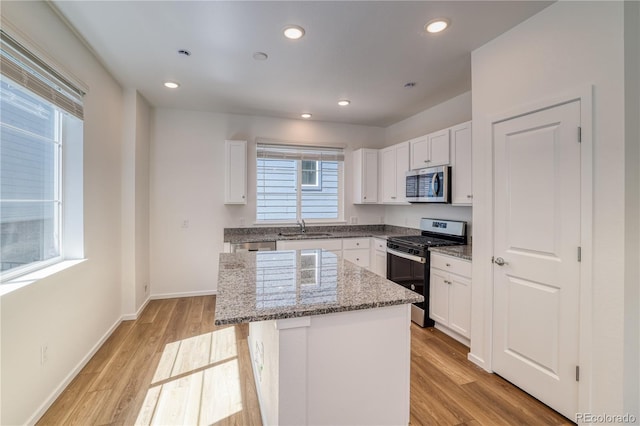 kitchen with a center island, white cabinets, sink, light wood-type flooring, and appliances with stainless steel finishes