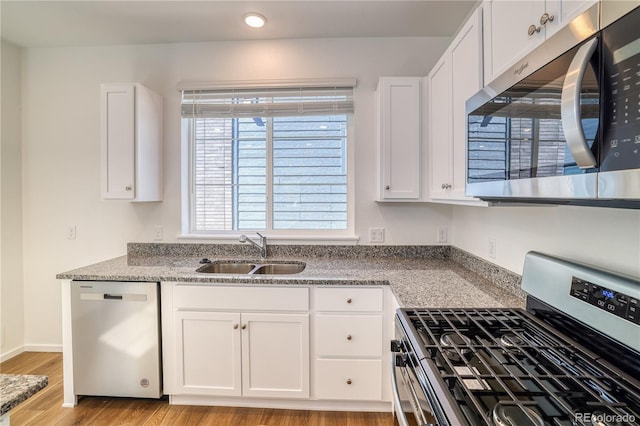 kitchen with white cabinetry, sink, stainless steel appliances, light stone counters, and light wood-type flooring