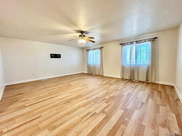 unfurnished room with light wood finished floors, ceiling fan, baseboards, and a textured ceiling