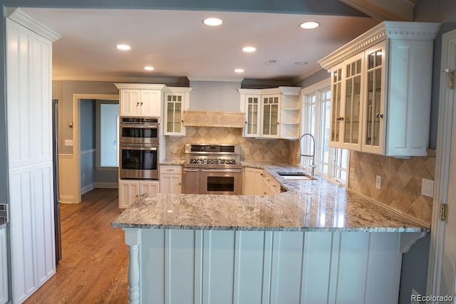 kitchen with appliances with stainless steel finishes, a sink, custom exhaust hood, ornamental molding, and a peninsula