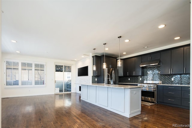 kitchen featuring appliances with stainless steel finishes, dark hardwood / wood-style flooring, light stone counters, decorative light fixtures, and a center island with sink