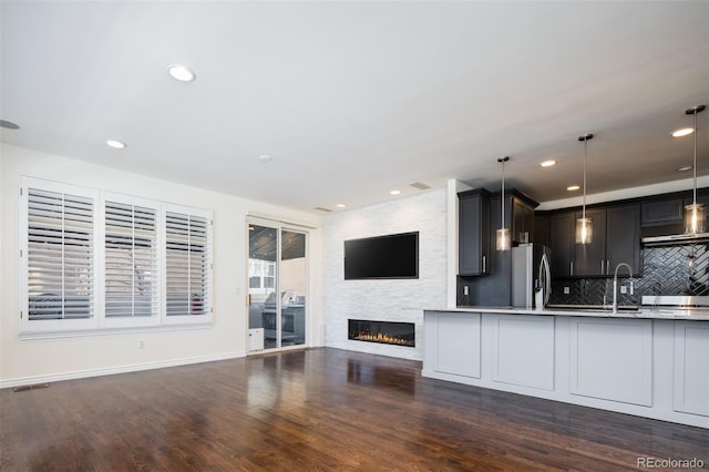 kitchen featuring pendant lighting, backsplash, dark wood-type flooring, a fireplace, and stainless steel fridge with ice dispenser