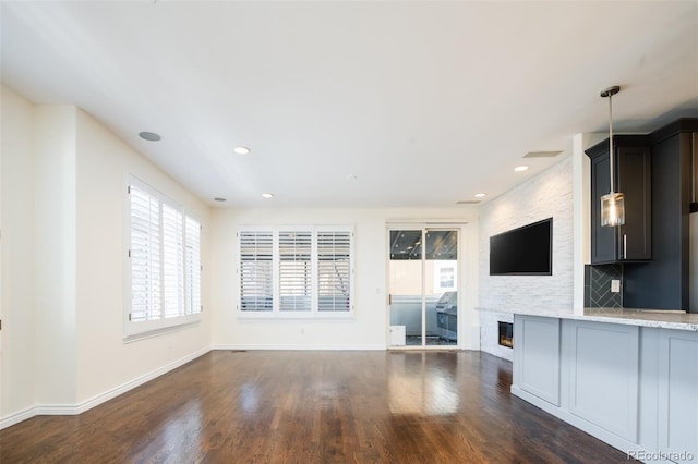 unfurnished living room with a stone fireplace and dark wood-type flooring