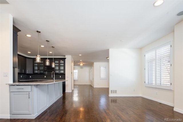 kitchen with pendant lighting, plenty of natural light, light stone countertops, and backsplash