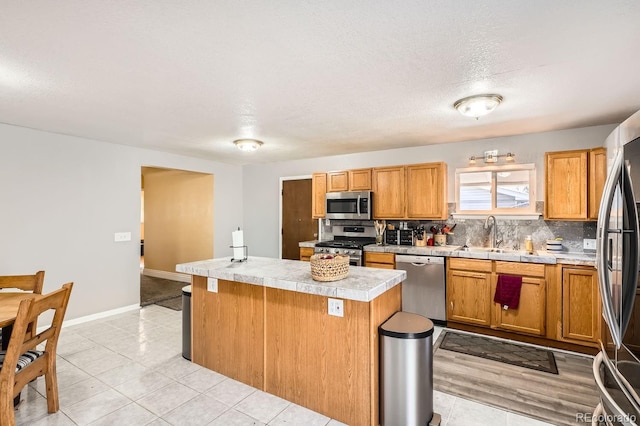 kitchen featuring sink, light tile patterned floors, backsplash, a kitchen island, and appliances with stainless steel finishes