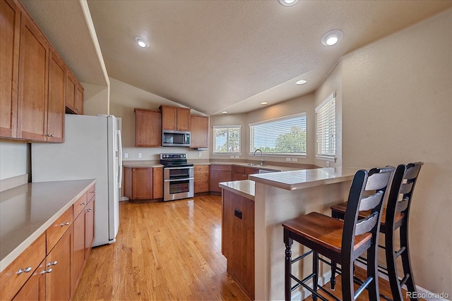 kitchen featuring sink, light hardwood / wood-style floors, vaulted ceiling, a breakfast bar, and appliances with stainless steel finishes