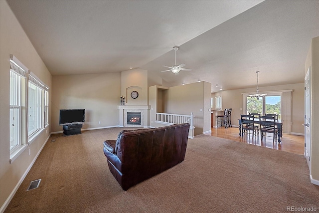 carpeted living room with ceiling fan with notable chandelier, a fireplace, and vaulted ceiling