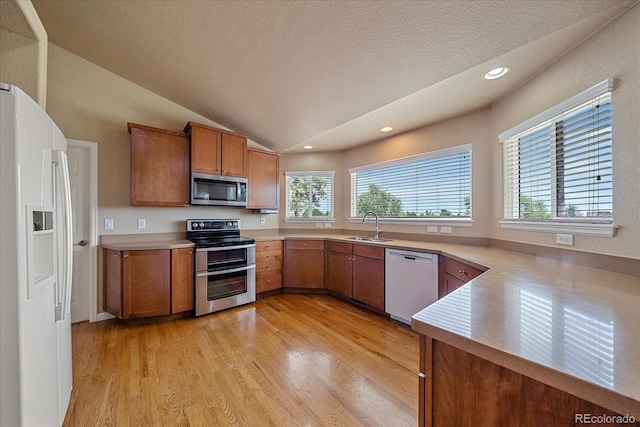 kitchen featuring sink, stainless steel appliances, light hardwood / wood-style floors, a textured ceiling, and lofted ceiling