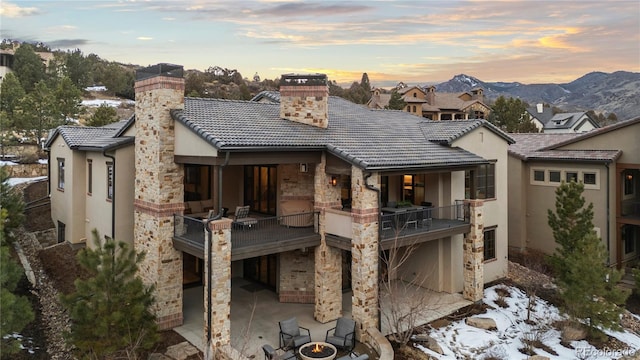 back of property with stone siding, a chimney, a tiled roof, a patio area, and stucco siding