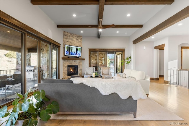 living area featuring light wood-style floors, recessed lighting, beam ceiling, and a stone fireplace