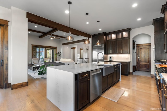 kitchen featuring light wood-style flooring, a sink, light countertops, appliances with stainless steel finishes, and beam ceiling