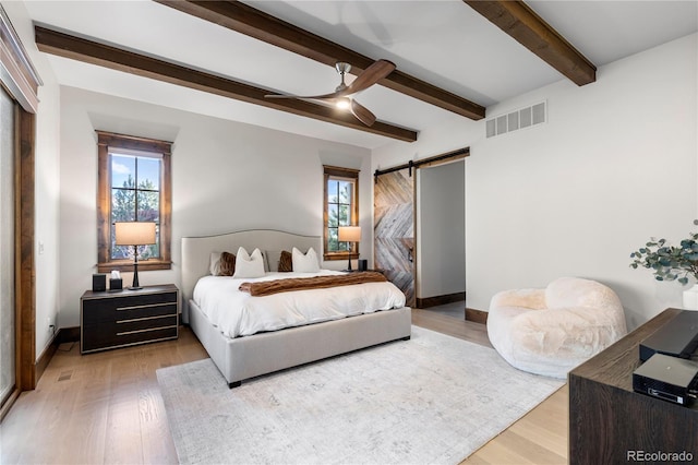 bedroom featuring a barn door, visible vents, baseboards, light wood-type flooring, and beam ceiling