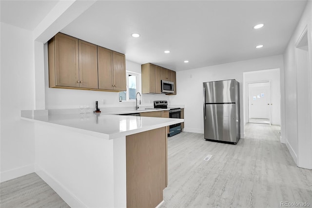 kitchen with stainless steel appliances, kitchen peninsula, sink, and light wood-type flooring